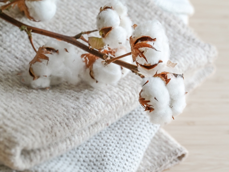 Branche ornée de boules de coton duveteuses sur un tas de tissus aux couleurs naturelles, concept de mode, culture écologique, transformation durable et commerce équitable, espace pour texte, mise au point sélective