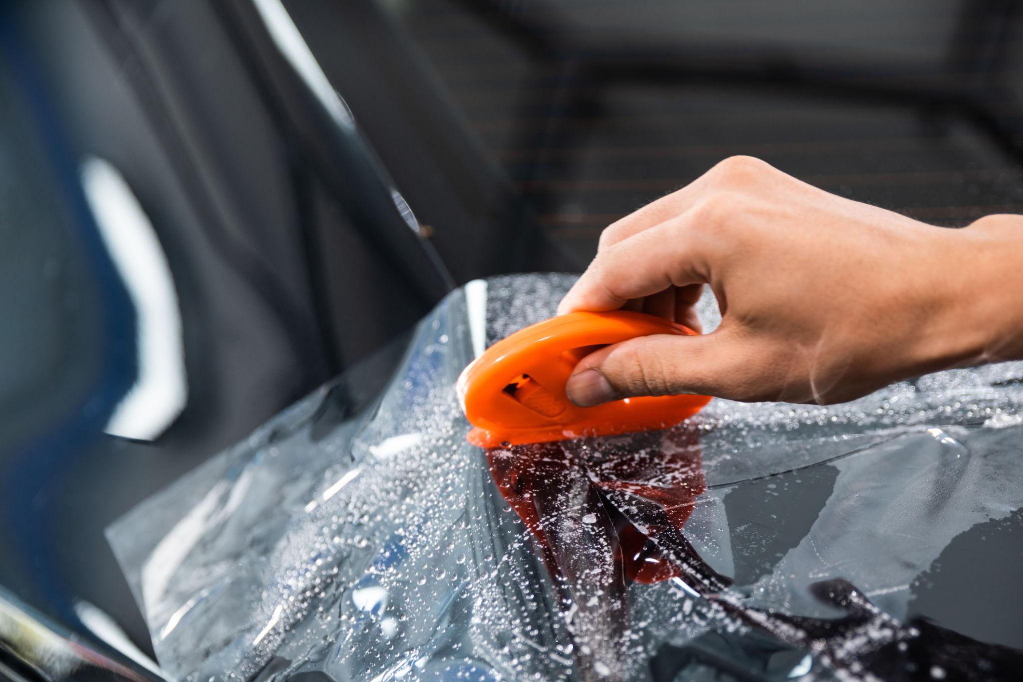 technician applying paint protection film manually on car surface