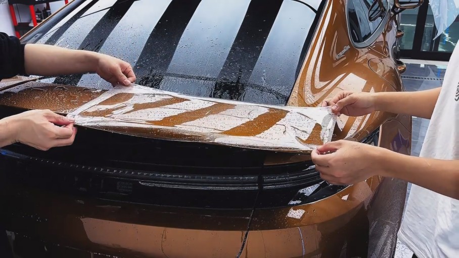 Des installateurs appliquent un film PPF prédécoupé sur le panneau arrière d'une voiture afin d'améliorer l'efficacité de la pose du film de protection de peinture.