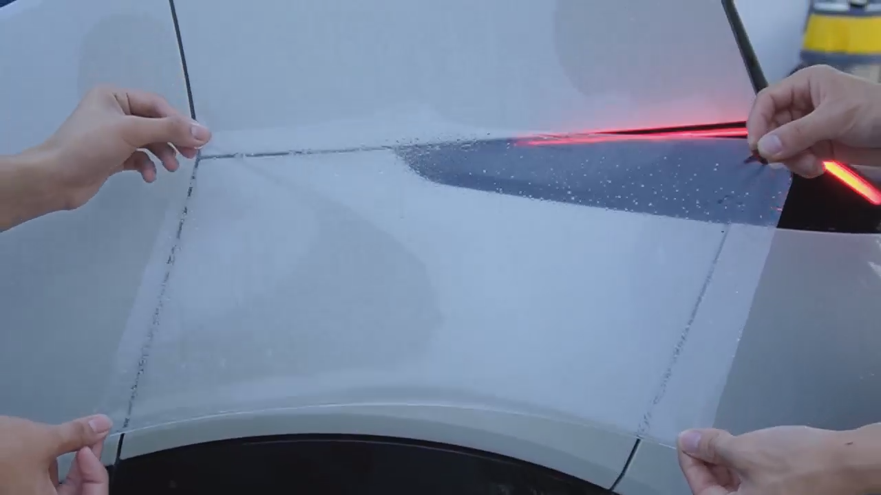Installers checking the fit of a pre-cut PPF pattern on a vehicle panel before installation