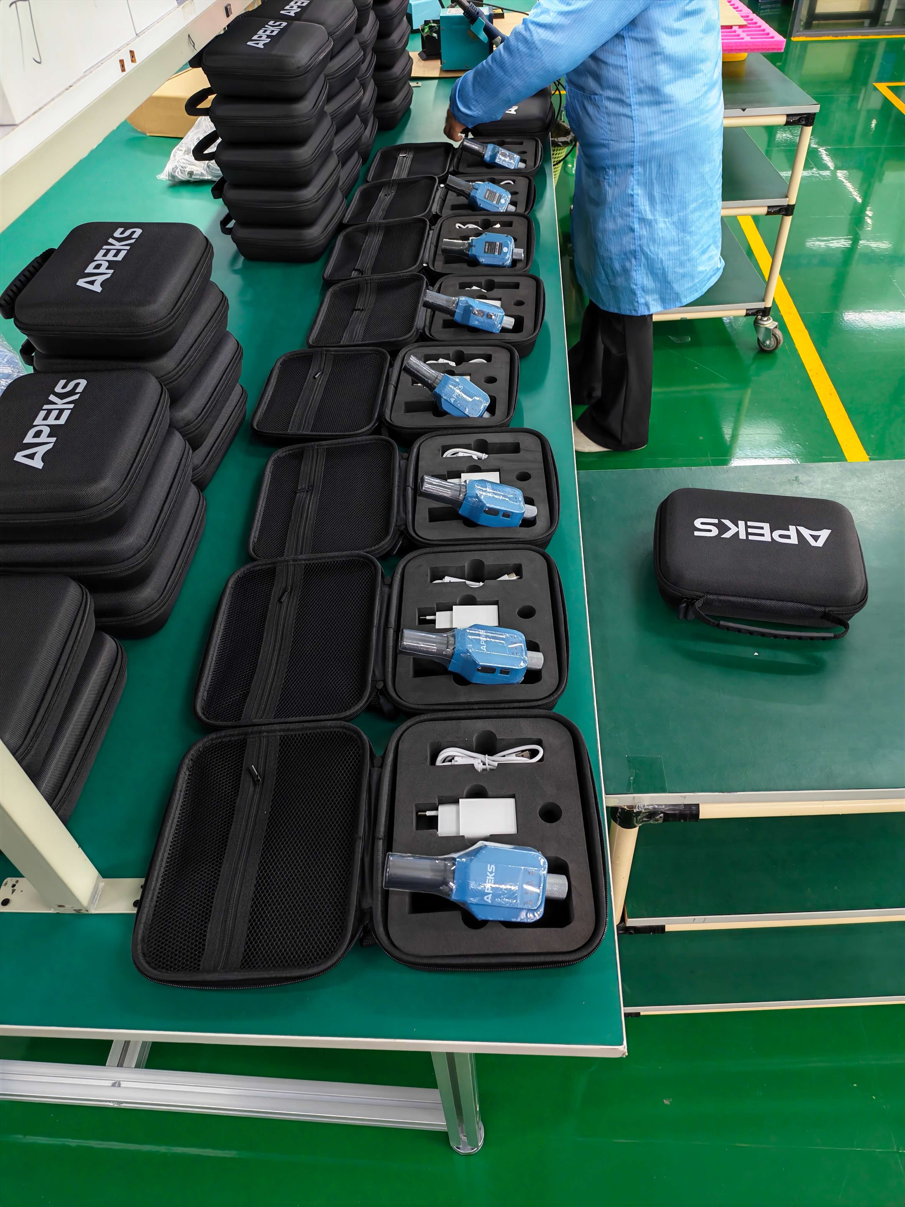 Factory worker packaging APEKS APS1 handheld RTK receivers with accessories into custom zippered carry cases
