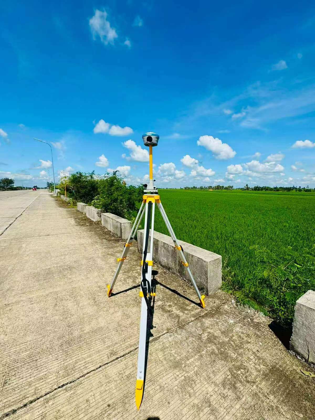 APEKS MAX5 GNSS base station setup on a survey tripod overlooking open agricultural fields for UAV RTK corrections