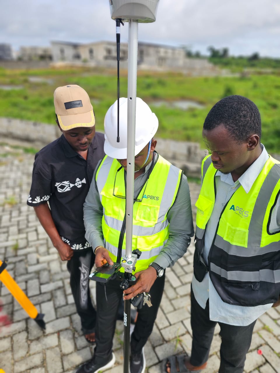 Field surveyors reviewing coordinate data on an APEKS rugged controller during an on-site RTK training session in Nigeria