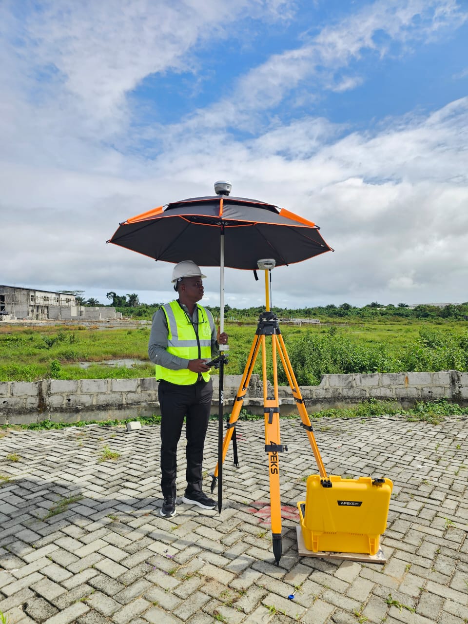 Surveyor operating APEKS RTK rover equipped with a protective survey sunshade umbrella alongside a tripod base station in Nigeria