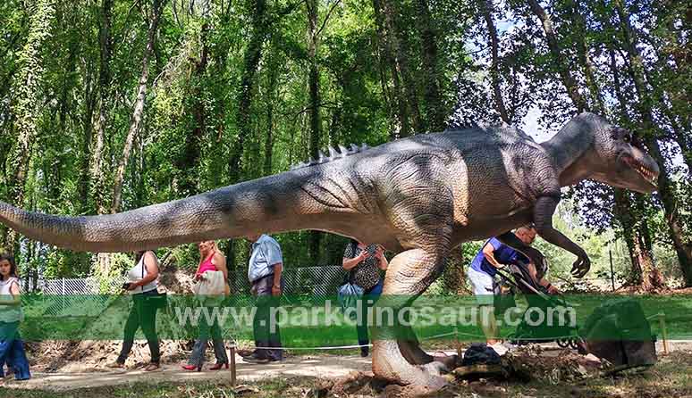 Gray life-size dinosaur displayed among mature trees in Lugo