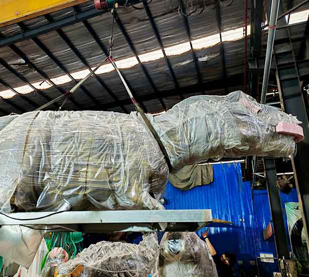 Wrapped dinosaur model being lifted during container loading