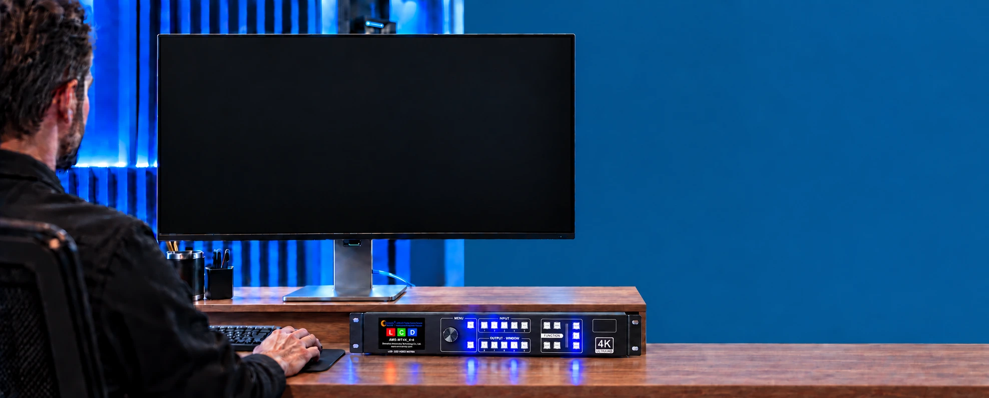 Technician using a wired desktop workstation with the AMS-MT4K matrix in a blue and amber control room