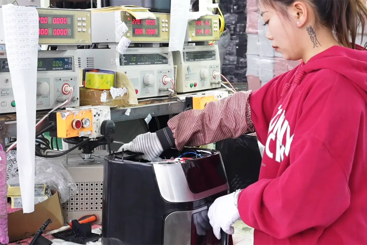 Worker assembling wiring and internal parts for an air fryer on the production line