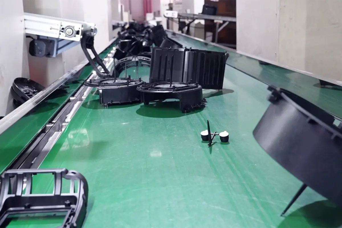 Black molded appliance plastic parts moving on a green conveyor belt after injection molding