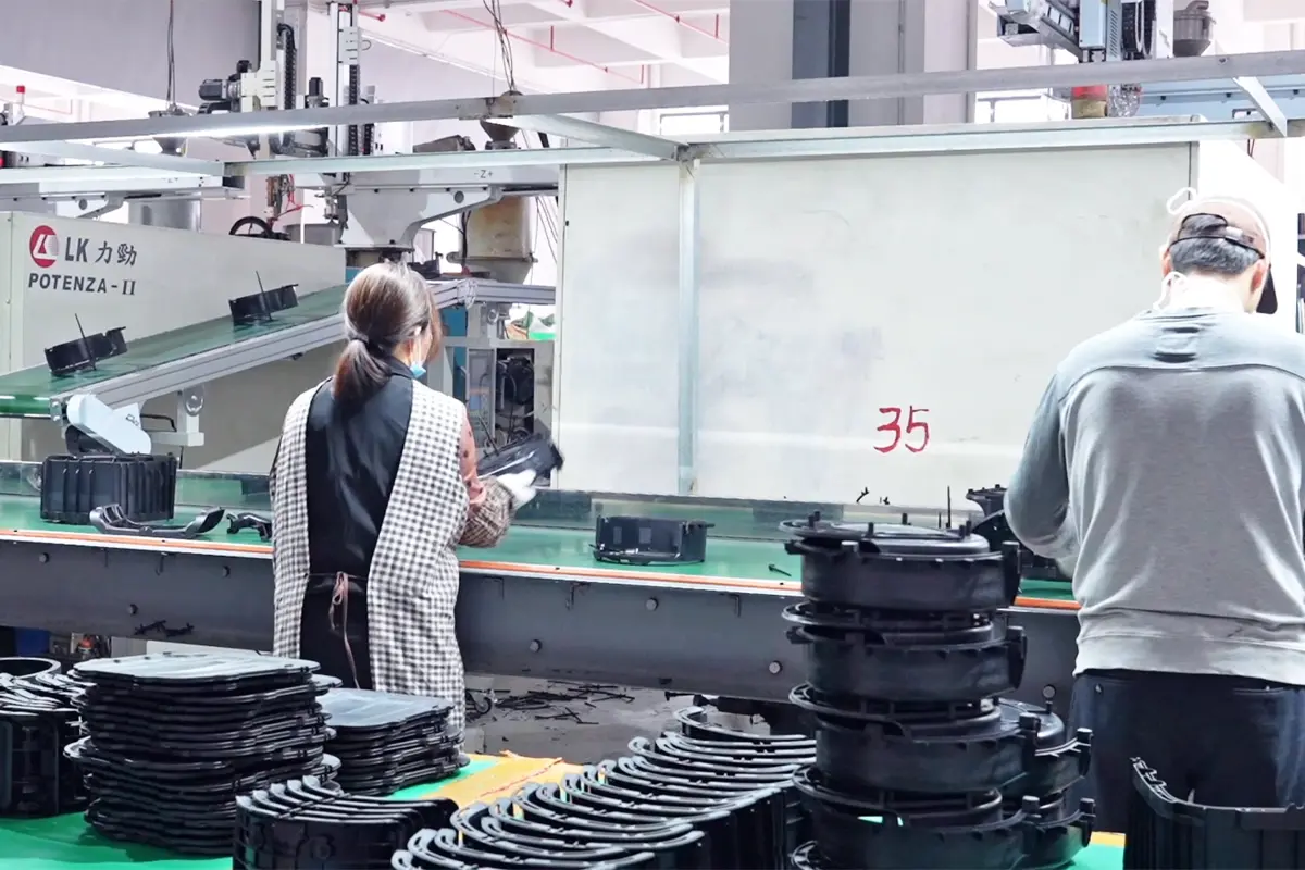 Workers checking and arranging molded black plastic appliance parts beside injection molding machines